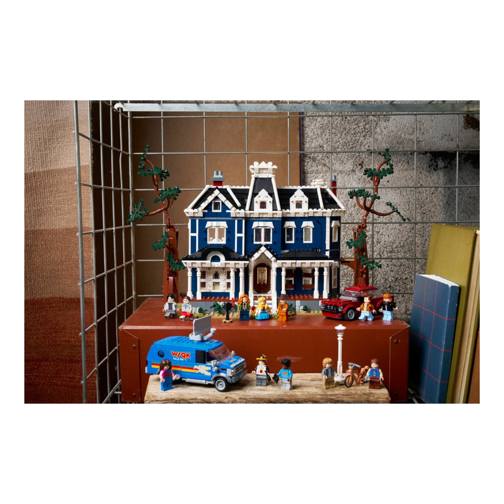Detailed model of LEGO Stranger Things: The Creel House with minifigures, vehicles, and trees on a shelf.